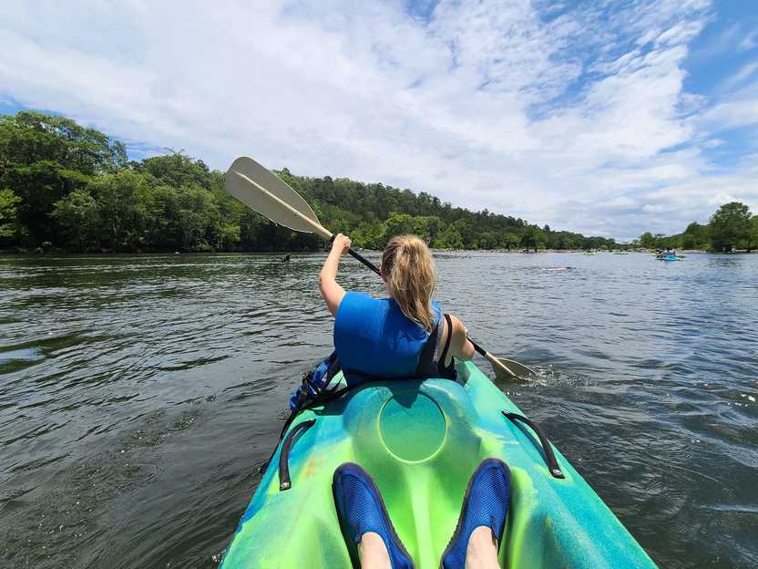 Lydia at the front of a tandem kayak paddling in Mountain Fork River.
