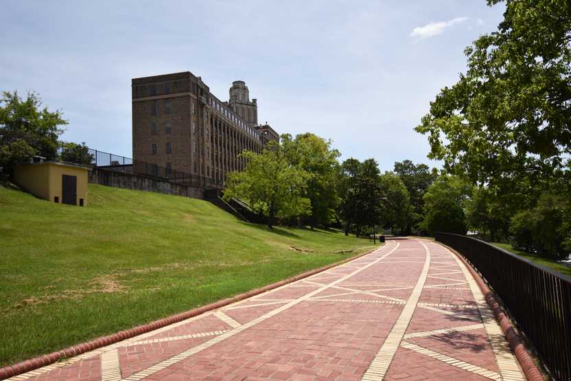 A wide, red and yellow brick promenade. There is a hill with a building on the left and a fence to the right. 