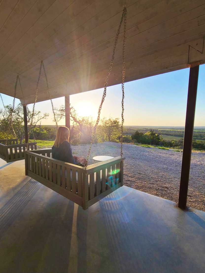 Lydia sitting on a swinging bench looking out at the sunset at Southold Farm and Cellar.