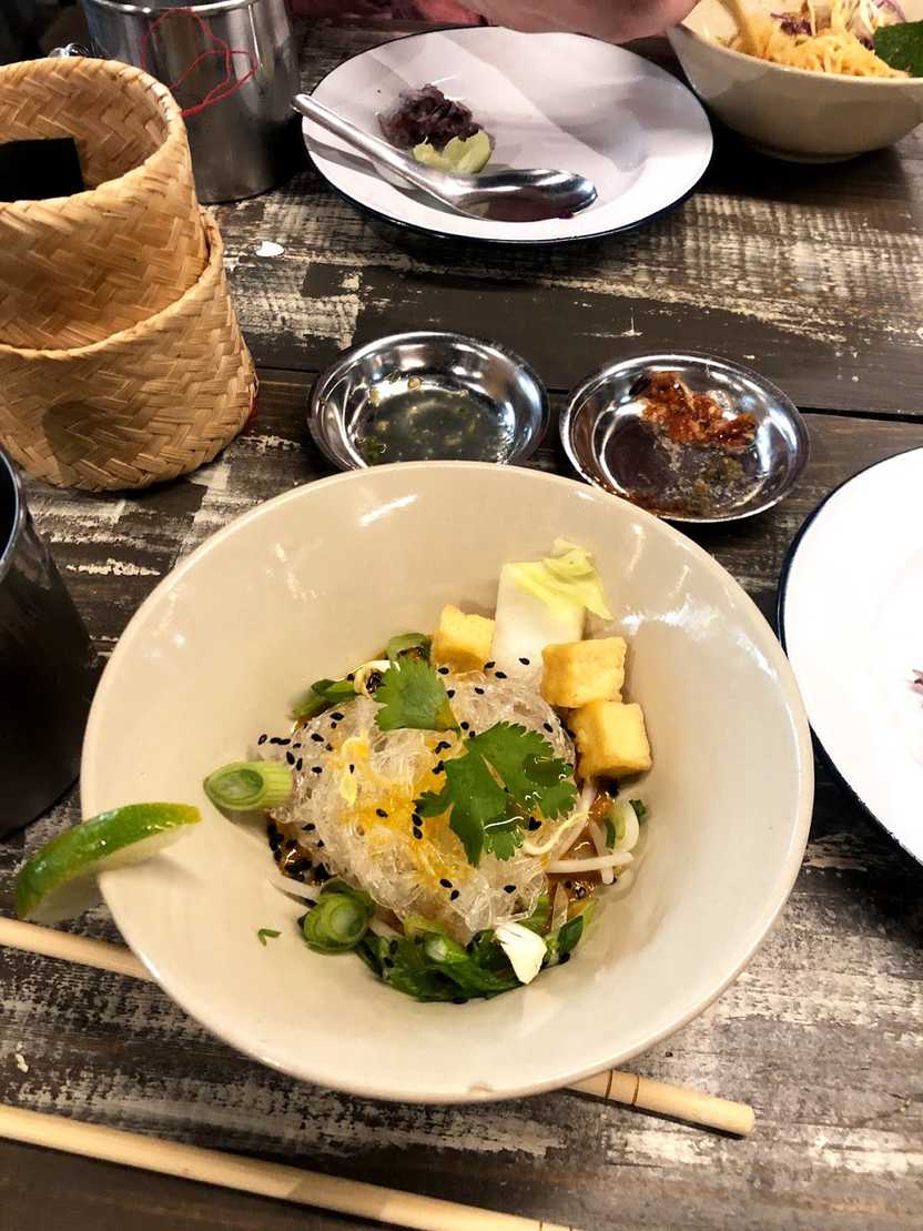 A small bowl with clear noodles, cilantro, sesame seeds and green onions.
