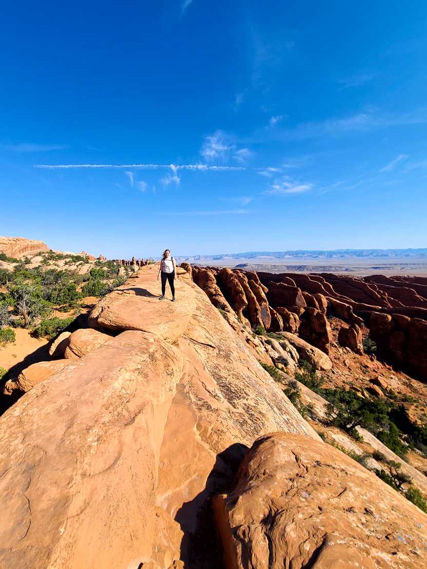 Lydia standing on top of a rock with rock spire views in the distance on the Devil's Garden trail.