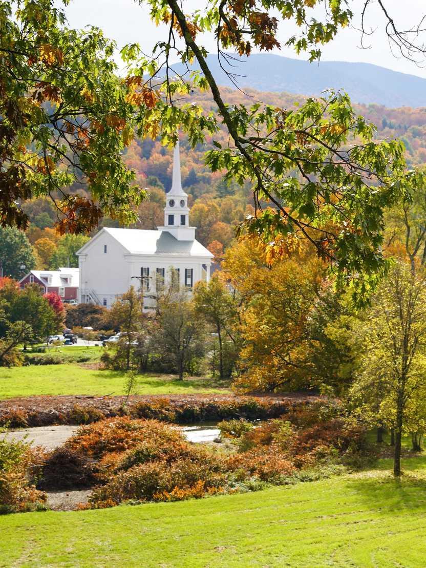A white church with mountains in the background and trees in the foreground.
