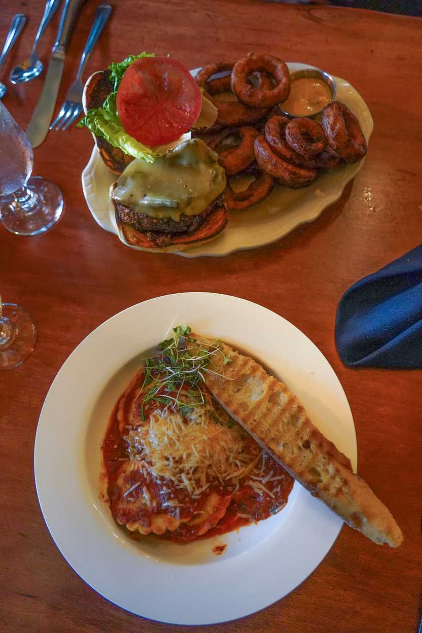 A plate of pasta and garlic bread, and a plate of onion rings and a burger.