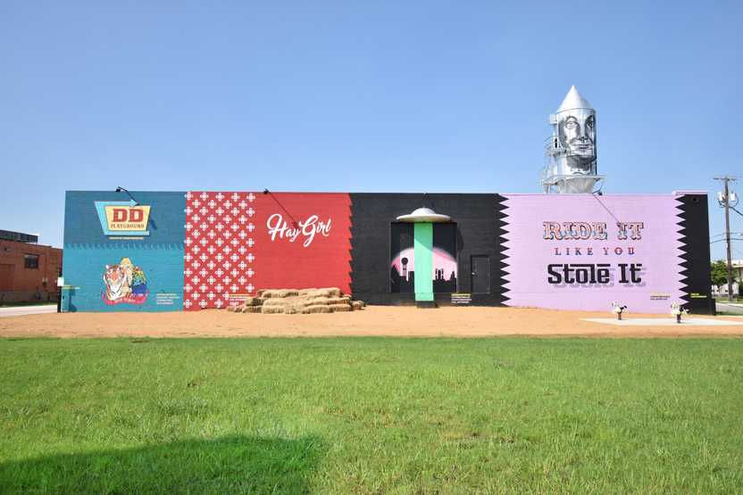 A wall of colorful murals, including one that says "Hay Girl" with hay bails below it and a pink wall that says "Ride it like you Stole It" with pony rides below it.