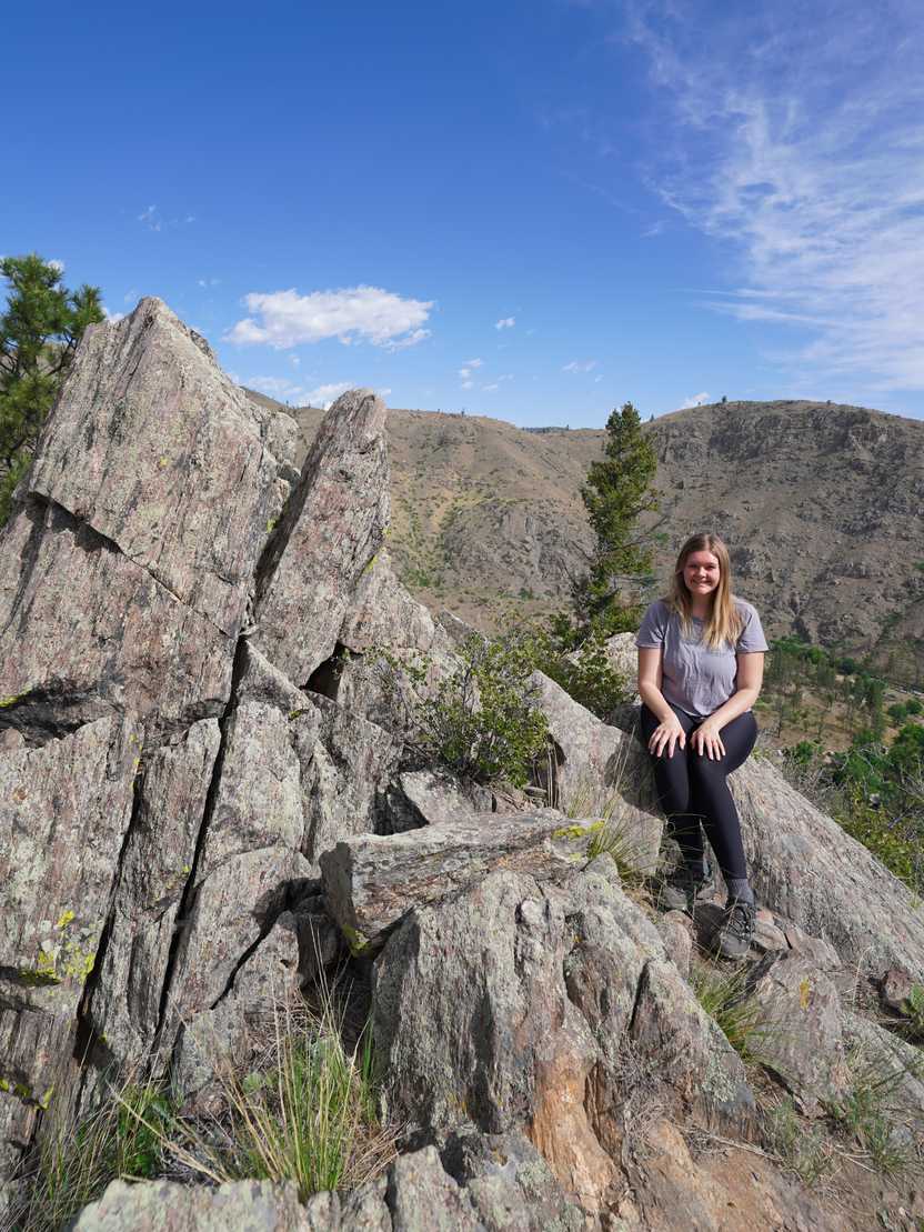 Lydia sitting on an area of black, jagged rocks along the Black Powder Trail in the Gateway Natural Area.