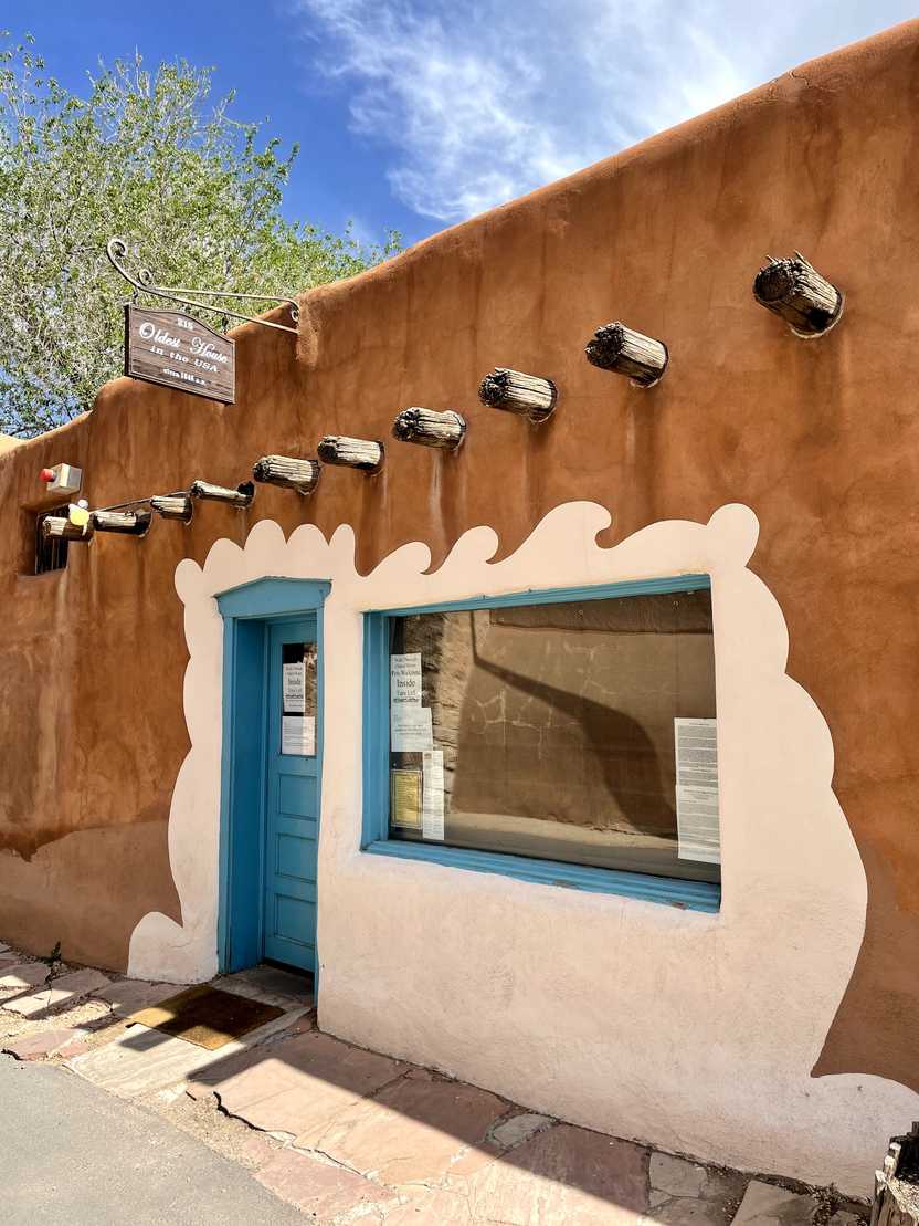 The exterior of the Oldest House in the US. It is painted a rust color with a white shape encompassing the door and window. The door is blue.